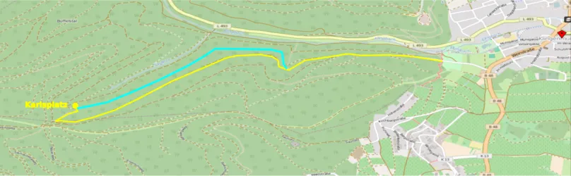 Eine Karte mit einem eingezeichneten Weg, der durch grüne Hügel führt. Der Weg ist in Blau und Gelb markiert und zeigt die Route zur Karolinenquelle.