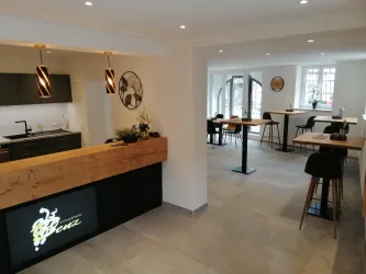 Ein modernes Café mit einer einladenden Theke aus Holz. Die helle Innenausstattung bietet Platz für mehrere Tische und Stühle.