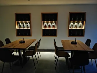 Ein gemütlicher Raum mit Holz-Tischen und Stühlen. An der Wand sind Regale mit Flaschen beleuchtet.