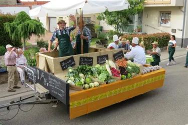 Ein festlicher Umzug mit einem Wagen voller frischem Gemüse. Menschen in Trachten winken und feiern entlang der Straße.