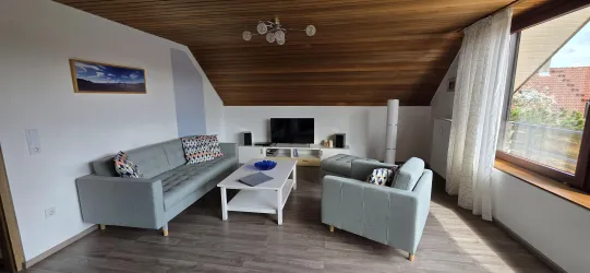 Ein gemütlicher Wohnraum mit grünem Sofas und einem Couchtisch. Große Fenster sorgen für viel Licht und Helligkeit.