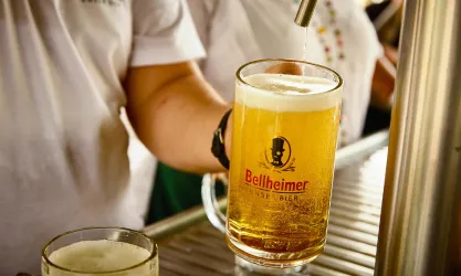 Ein Glas Bier wird gezapft, während eine Hand den Zapfhahn bedient. Im Hintergrund sind weitere Biergläser sichtbar.