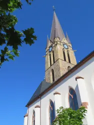 Ein hoher Kirchturm ragt gegen den klaren blauen Himmel. Die Kirche hat eine helle Fassade und wunderschöne Fenster.