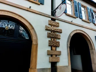 Ein historisches Gebäude mit einem dekorativen Holzschild. Die Fenster sind mit blauen Läden versehen.