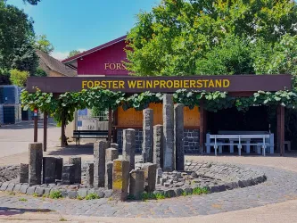 Ein Weinstand mit einem überdachten Bereich und einer auffälligen Beschilderung. Umgeben von Pflanzen und einer gemütlichen Atmosphäre.