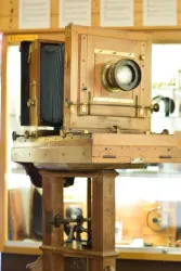 Eine alte Holzklinikamera steht auf einem stabilen Stativ. Im Hintergrund sind weitere historische fotografische Geräte sichtbar.