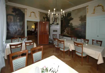 Ein eleganter Speisesaal mit einem Holzfußboden und kunstvollen Wandmalereien. Tische sind schön gedeckt und der Raum ist gut beleuchtet.