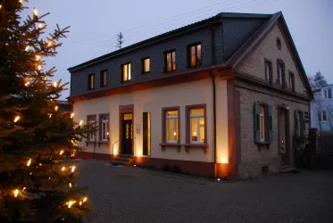 Ein modernes Gebäude mit warm beleuchteten Fenstern. Im Vordergrund steht ein Lichtbaum, der eine festliche Atmosphäre schafft.