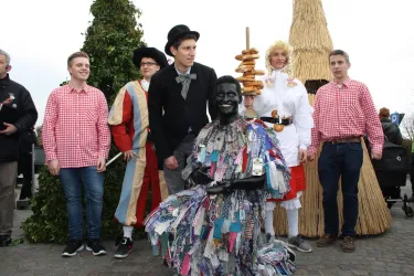 Eine Gruppe von Menschen in traditionellen Kostümen steht auf einer Feier. Im Vordergrund sitzt eine Person in einem bunten kostümierten Outfit.