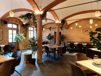 Ein modernes Restaurant mit Holztischen und bequemen Stühlen. Die Wände sind mit Pflanzen und stilvollen Lampen dekoriert.