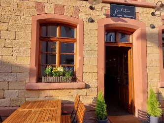 Ein gemütliches Restaurant mit einer einladenden Außenterrasse. Die Fenster sind mit bunten Blumen geschmückt und die Fassade ist aus Naturstein.