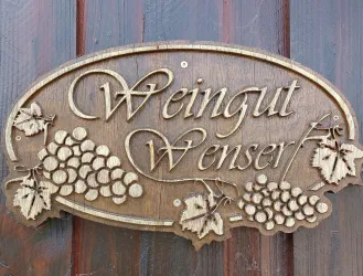 Ein Holzschild mit der Aufschrift "Weingut Wenser". Es sind auch Trauben und Blätter eingraviert.