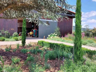 Ein gepflegter Garten mit verschiedenen Pflanzen und Kräutern. Im Hintergrund steht eine hölzerne Scheune, die teilweise geöffnet ist.