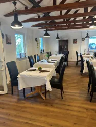 Ein einladendes Restaurant mit hellen Tischen und schwarzen Stühlen. Die Holzbalkendecke und das warme Licht schaffen eine gemütliche Atmosphäre.