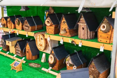 Eine Reihe von bunten Vogelhäusern aus Holz steht auf einem Regal. Die Vogelhäuser haben unterschiedliche Designs und sind auf grünem Gras ausgelegt.
