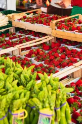 Frische Erdbeeren in Holzkisten und grüner Spargel auf einem Marktstand. Bunte Farben und eine einladende Atmosphäre.