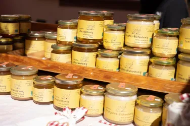 Eine Auswahl an Honiggläsern auf einem Holzregal. Jedes Glas hat ein gelbes Etikett mit Informationen über den Inhalt.