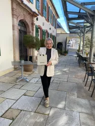 Eine Person geht durch einen hellen Innenhof und trägt eine Einkaufstasche. Die Umgebung hat viele Pflanzen und moderne Architektur.