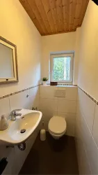 Ein kleines, modernes Badezimmer mit einem Waschbecken und einer Toilette. Der Raum hat eine Holzbalkendecke und ein Fenster mit Blick nach draußen.