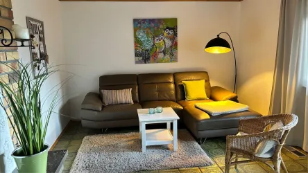 Ein gemütliches Wohnzimmer mit einer modernen, grauen Couch und einem Beistelltisch. An der Wand hängt ein farbenfrohes Gemälde und eine Stehlampe sorgt für warmes Licht.