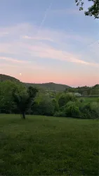 Eine ruhige Landschaft mit sanften Hügeln und einem klaren Himmel. Der Sonnenuntergang färbt die Wolken in zarten Rosa- und Blautönen.