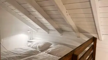 Ein gemütliches Schlafzimmer im Dachgeschoss mit zwei Betten. Die Wände und das Holzgebälk sind in hellen Farben gehalten.