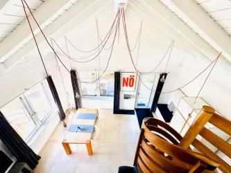 Ein modernes Wohnzimmer mit hohen Decken und großen Fenstern. Ein Tisch und Stühle sind im Raum, während von der Decke rote Kabel hängen.