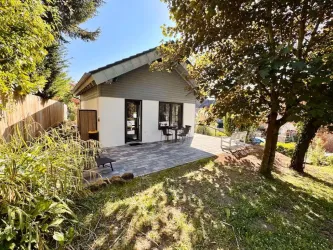 Ein modernes Häuschen umgeben von grünem Gras und Bäumen. Eine Terrasse mit Stühlen lädt zum Entspannen ein.