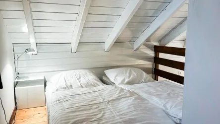 Ein gemütliches Schlafzimmer mit einem Doppelbett und weißen Bettwaren. Die Decken sind aus Holz und verleihen dem Raum eine helle, einladende Atmosphäre.