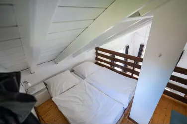 Ein gemütliches Schlafzimmer unter einem schrägen Dach mit zwei Betten. Die Wände sind weiß und der Boden ist aus Holz.