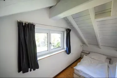 Ein gemütliches Schlafzimmer mit einem Dachfenster und aufgeräumtem Bett. Die Wände sind weiß und die Vorhänge sind dunkel, was einen angenehmen Kontrast schafft.