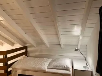 Ein gemütliches Schlafzimmer mit einem Einzelbett und anschließenden Möbeln. Die Wände und Decke sind weiß gestrichen, und das Dach hat schräge Linien.