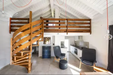 Ein modernes Wohnzimmer mit einer spiralförmigen Holztreppe. Hell und einladend, mit einer offenen Küche und zwei gemütlichen Sesseln.