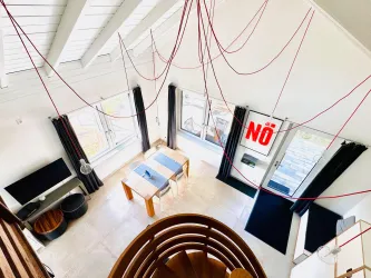 Blick von der Empore, wo sich der Schlafbereich befindet in den modernen Wohn-Essbereich mit großen Fenstern und viel Tageslicht.