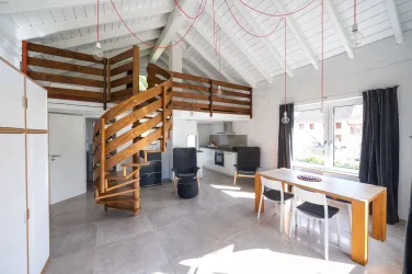 Eine moderne Wohnung mit einem offenen Wohnbereich und einer Wendeltreppe zum Schlafbereich. Große Fenster sorgen für viel Tageslicht und eine helle Atmosphäre.