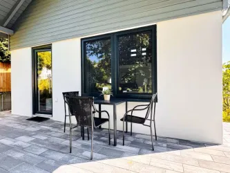 Eine moderne Terrasse mit einem Tisch und vier Stühlen. Die großen Fenster lassen viel Licht herein und bieten einen Blick ins Freie.