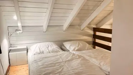 Ein gemütliches Schlafzimmer mit einem Doppelbett und weißen Bettdecken. Die schrägen Decken und der Holzboden verleihen dem Raum ein warmes, einladendes Ambiente.