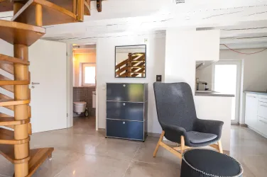 Ein modernes Wohnzimmer mit einer Wendeltreppe zum Schlafbereich und gemütlichen Sesseln. Hell und lichtdurchflutet. Neben einem CD-Radio und einem Smart-TV gibt es im ganzen Haus und auf der Terrasse stabiles WLAN.