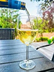 Ein Glas mit sprudelndem Getränk wird von einer Flasche eingegossen. Der Hintergrund zeigt eine grüne Gartenlandschaft.