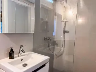 Ein modernes Badezimmer mit einer Dusche und einem eleganten Waschbecken. Die Wände sind hell gefliest und es gibt einen Spiegelschrank.