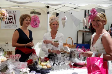 Drei Frauen stehen an einem Marktstand und lächeln. Der Stand ist festlich dekoriert und bietet verschiedene Leckereien und Accessoires an.