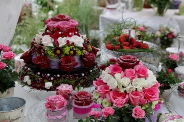 Ein wunderschöner Tisch mit üppigen Blumenarrangements in verschiedenen Rosatönen. Im Mittelpunkt stehen kunstvoll dekorierte Torten aus Blumen.