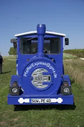 Eine blaue Lokomotive steht auf einer Wiese. Der Himmel ist klar und blau.