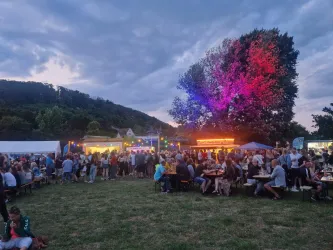 Eine lebhafte Veranstaltung im Freien mit vielen Menschen. Bunte Lichter und Stände schaffen eine festliche Atmosphäre.