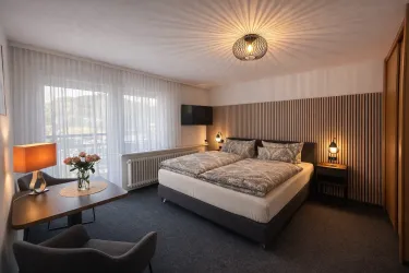 Ein modernes Schlafzimmer mit einem komfortablen Doppelbett und einem stilvollen Tisch. Die große Fensterfront bringt viel Tageslicht hinein und schafft eine einladende Atmosphäre.