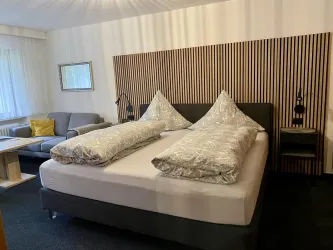 Ein modernes Hotelzimmer mit einem Doppelbett und zwei großen Kissen. Es gibt auch eine gemütliche Sitzecke mit einem Sofa und einem Tisch.