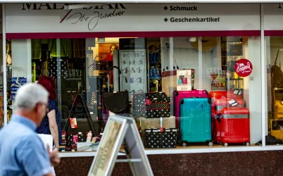 Ein Schaufenster mit bunten Reisekoffern und Schmuckartikeln. Im Vordergrund geht eine Person vorbei.