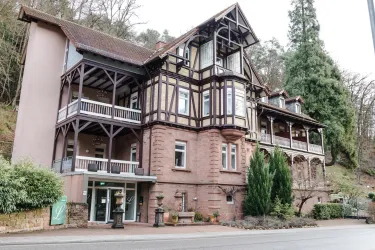 Ein historisches Gebäude im Fachwerkstil mit mehreren Etagen. Umgeben von Bäumen und einer grünen Landschaft.