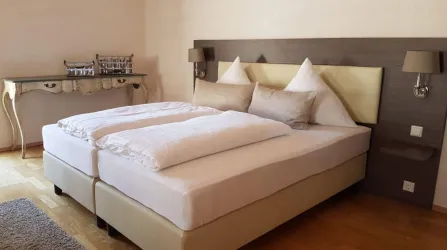 Ein modernes Schlafzimmer mit einem großen Doppelbett und weichen Kissen. An der Wand sind zwei Nachttischlampen und ein eleganter Tisch zu sehen.