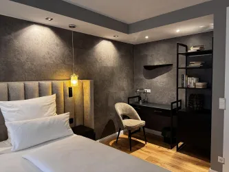 Ein modernes Schlafzimmer mit einer stilvollen Kopfstütze und einem komfortablen Stuhl. Der Raum hat warmes Licht und eine schlichte, elegante Einrichtung.